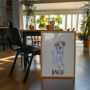 May include: A framed print featuring a line drawing of a white dog with a brown ear patch and a wine glass balanced on its head. The dog wears a collar, and the name KALLIE is printed in black capital letters at the bottom of the image.