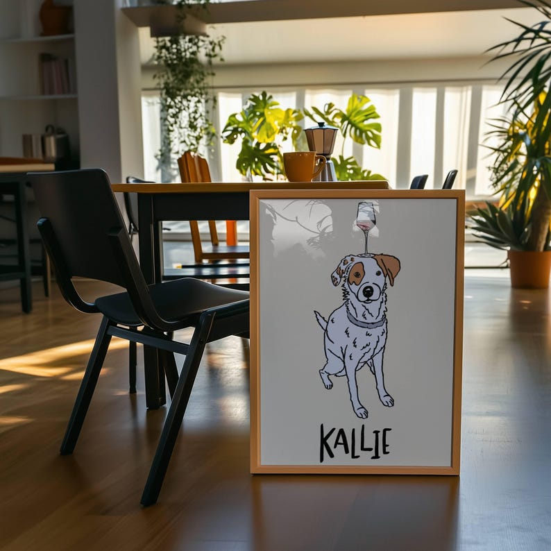 May include: A framed print featuring a line drawing of a white dog with a brown ear patch and a wine glass balanced on its head. The dog wears a collar, and the name KALLIE is printed in black capital letters at the bottom of the image.