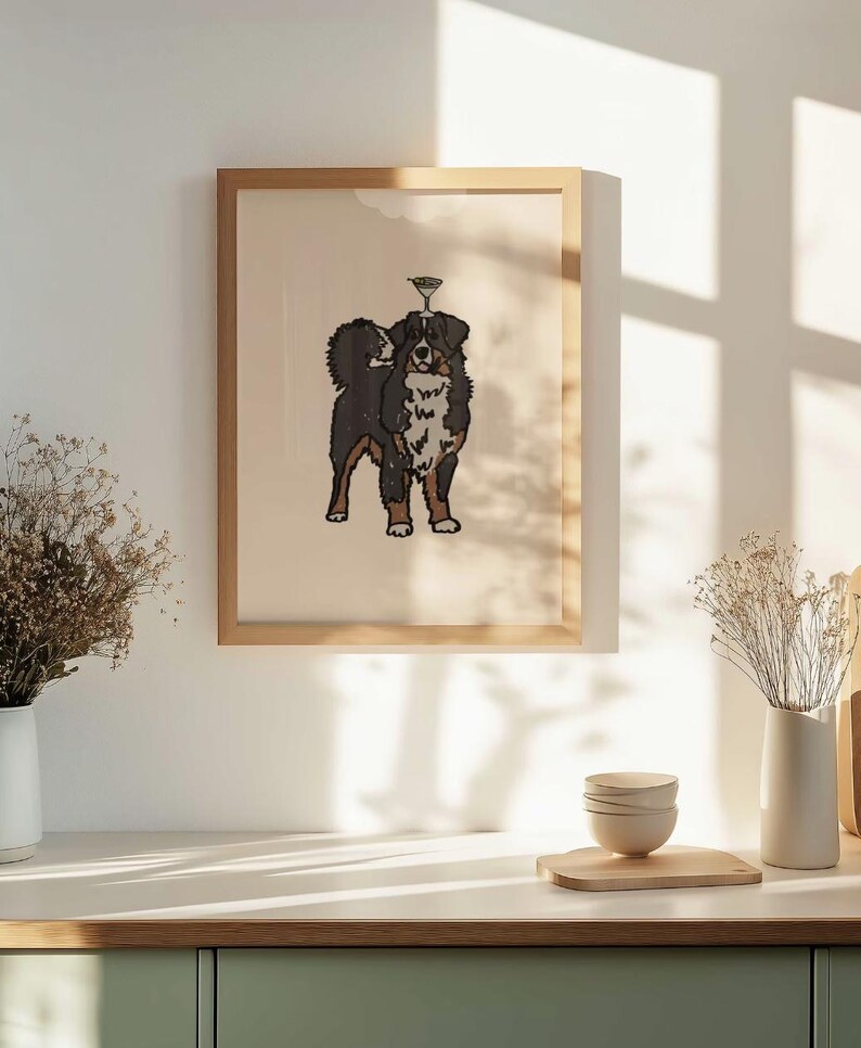 May include: A framed wall art print featuring a stylized illustration of a Bernese Mountain Dog with a martini glass balanced on its head. The dog has black, white, and brown fur, and the artwork is set against a light beige background.