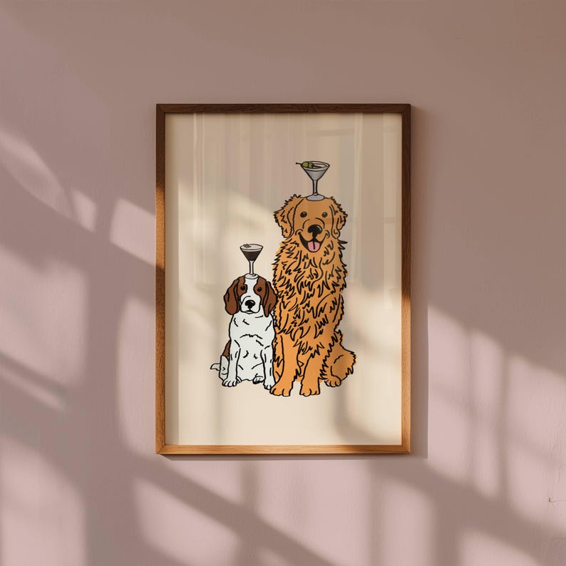 May include: A framed wall art print featuring a brown and white dog sitting next to a large golden-coloured dog. Each dog has a martini glass balanced on its head. The illustration is rendered in a clean, outlined style on a cream background.