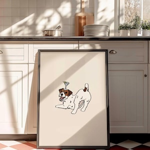 May include: A framed rectangular print featuring a white and brown Jack Russell terrier in a playful pose with a martini glass balanced on its head. The dog has a black nose, open mouth, and a brown patch over one eye, set against a cream background.