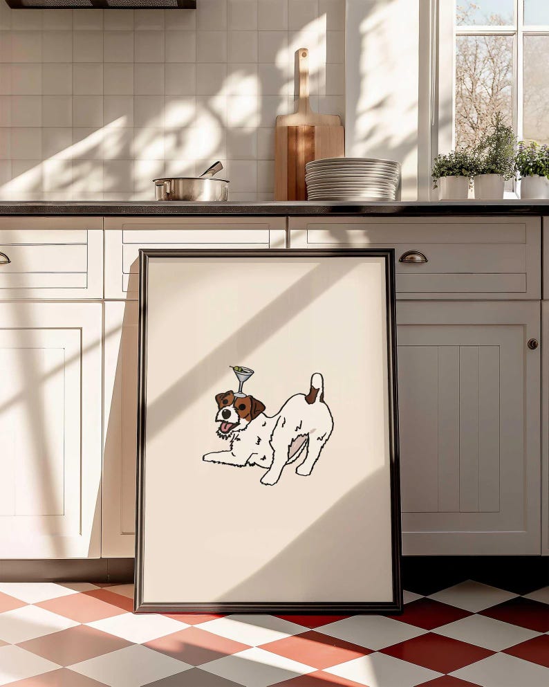 May include: A framed rectangular print featuring a white and brown Jack Russell terrier in a playful pose with a martini glass balanced on its head. The dog has a black nose, open mouth, and a brown patch over one eye, set against a cream background.
