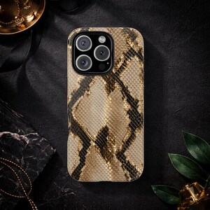 May include: A phone case with a snakeskin pattern in shades of tan, brown, and black. The case has a rectangular shape with rounded corners and a camera cutout. The case is designed to fit a smartphone.