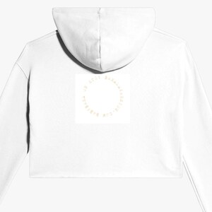 May include: White cropped hoodie with a hood. The back of the hoodie features a circular design with text. The hoodie is a casual garment, suitable for everyday wear. The design is centered on the back of the hoodie.