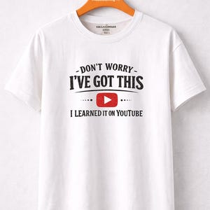Pode incluir: Camiseta branca com o texto "DON'T WORRY - I'VE GOT THIS" acima de um botão de reprodução do YouTube vermelho e o texto "I LEARNED IT ON YOUTUBE". A camiseta está pendurada em um cabide de madeira.