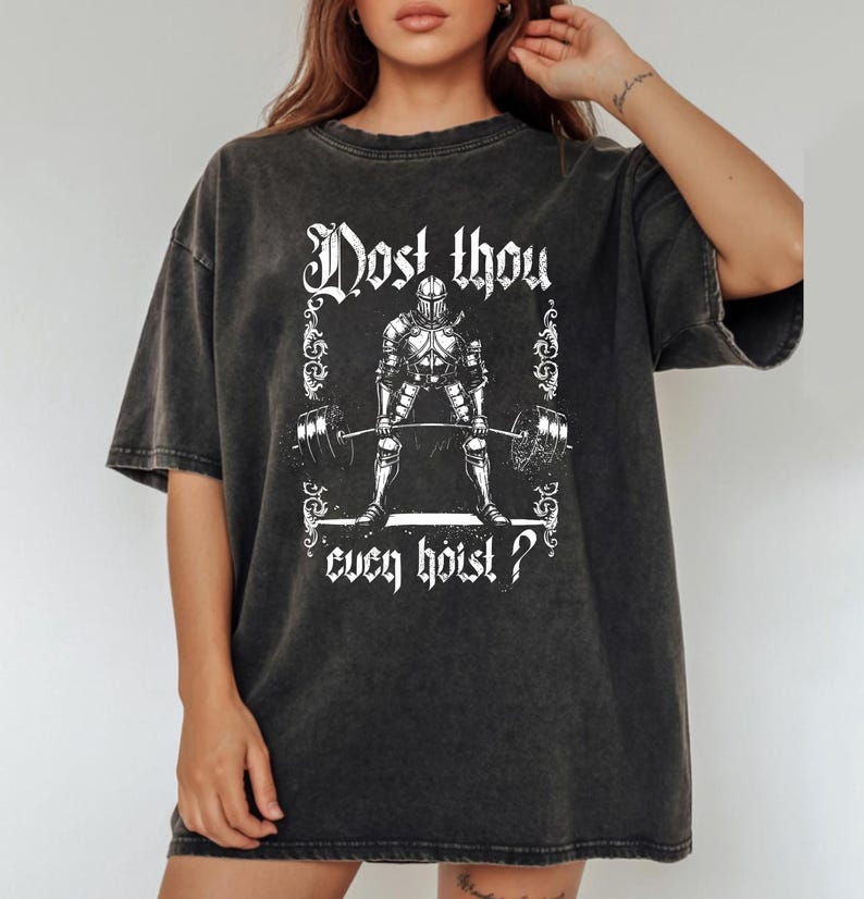 May include: Dark grey t-shirt featuring a white graphic of a knight lifting a barbell. The text "Dost thou even hoist?" is printed above and below the knight illustration. The shirt has a vintage, washed appearance.
