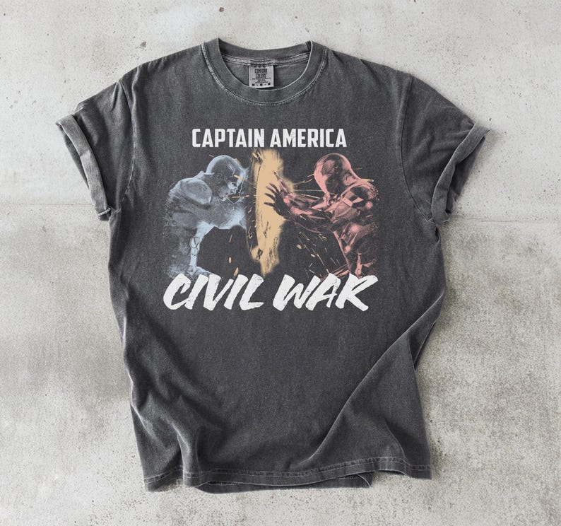 May include: Dark gray t-shirt featuring a graphic from Captain America: Civil War. The design shows two figures in action, with the words "CAPTAIN AMERICA" above and "CIVIL WAR" below in white. The shirt has a vintage, worn look.