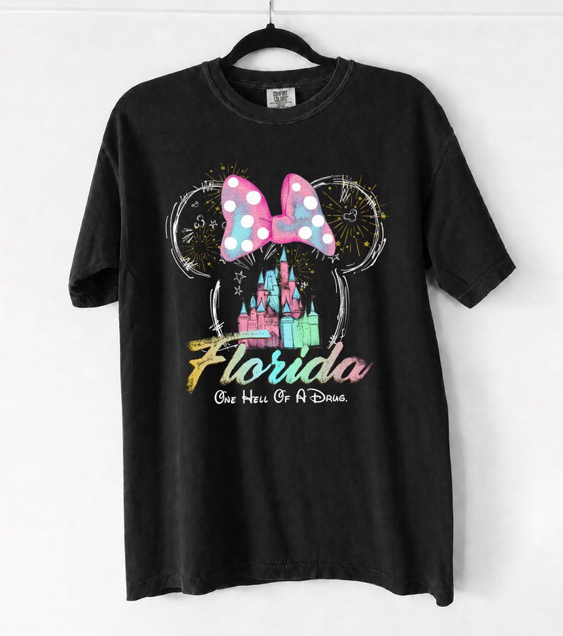 May include: Black t-shirt featuring a colorful graphic of a castle, a polka-dot bow, and the word "Florida" in a rainbow gradient. The text "One Hell Of A Drug" is below the word Florida.