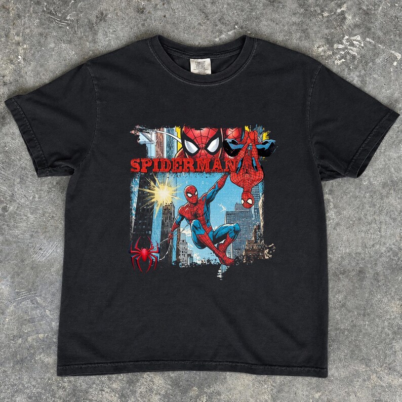 Puede incluir: Camiseta negra con un gr&aacute;fico colorido de Spider-Man. El dise&ntilde;o muestra a Spider-Man en poses de acci&oacute;n, con la palabra "SPIDERMAN" en rojo. El fondo representa un paisaje urbano. La camiseta tiene cuello redondo.