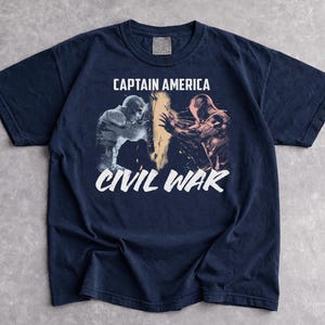 May include: Navy blue t-shirt featuring a graphic from Captain America: Civil War. The design shows two figures in action, with the words "CAPTAIN AMERICA" above and "CIVIL WAR" below in white text. The shirt is made of a soft material.