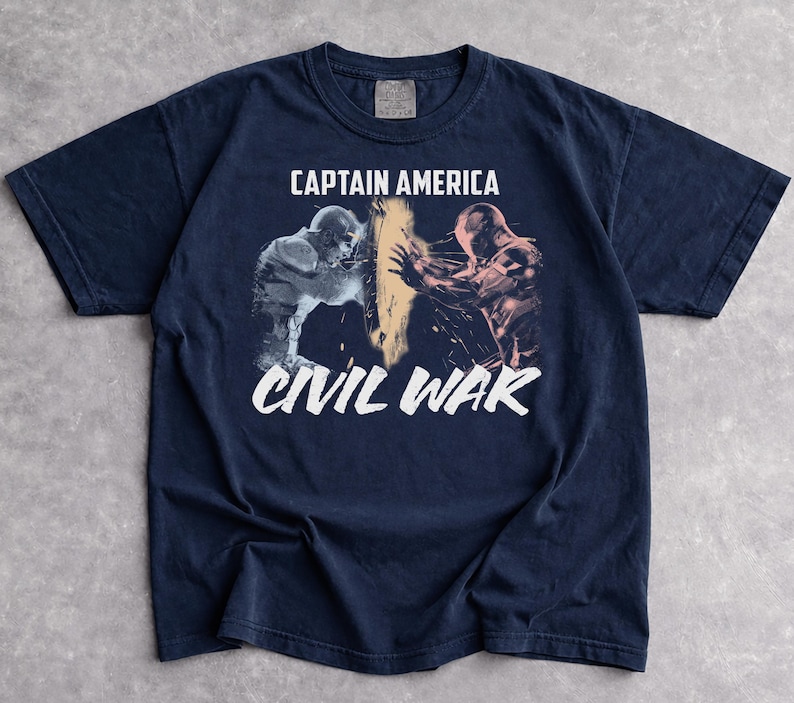May include: Navy blue t-shirt featuring a graphic from Captain America: Civil War. The design shows two figures in action, with the words "CAPTAIN AMERICA" above and "CIVIL WAR" below in white text. The shirt is made of a soft material.