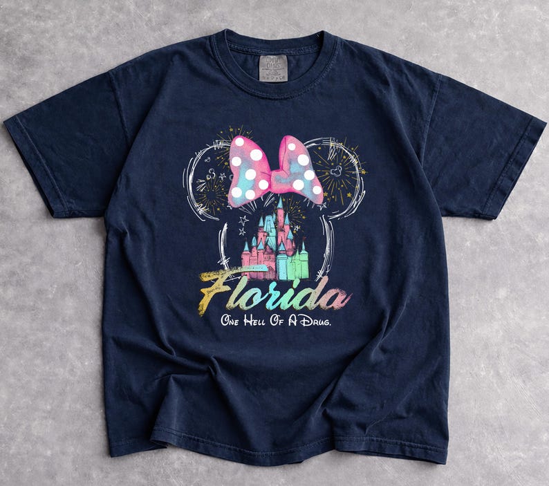 May include: Navy blue t-shirt featuring a Minnie Mouse design with a pink polka dot bow, a castle, and the word "Florida". The text "One Hell Of A Drug" is below the word Florida. The design is in white, pink, blue, and green.