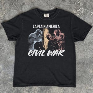 May include: Black t-shirt featuring the text "CAPTAIN AMERICA" above a graphic of two figures and the text "CIVIL WAR" in white. The graphic depicts a battle scene with figures in shades of blue and red.