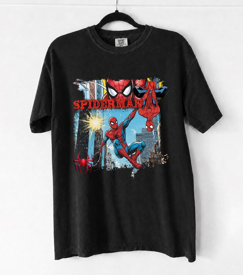 Puede incluir: Camiseta negra con un gr&aacute;fico colorido de Spider-Man en acci&oacute;n, con la palabra "SPIDERMAN" en rojo. El dise&ntilde;o incluye a Spider-Man en un paisaje urbano, con una telara&ntilde;a y una ara&ntilde;a.