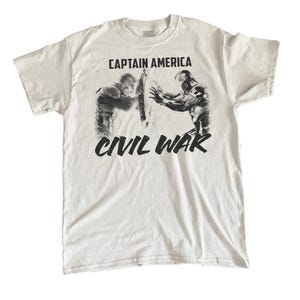 May include: White t-shirt featuring a graphic from Captain America: Civil War. The design shows Captain America and Iron Man in a battle pose, with the words "CAPTAIN AMERICA" above and "CIVIL WAR" below in black.