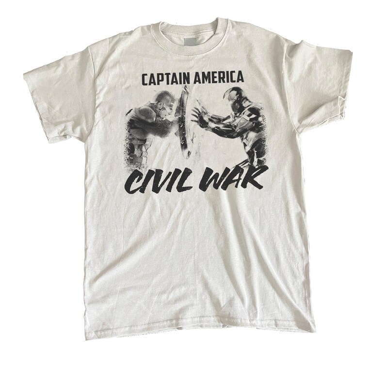 May include: White t-shirt featuring a graphic from Captain America: Civil War. The design shows Captain America and Iron Man in a battle pose, with the words "CAPTAIN AMERICA" above and "CIVIL WAR" below in black.