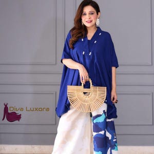 May include: A woman wearing a cobalt blue tunic with white accents and matching wide-leg pants with a blue and white floral pattern. She is holding a light brown bamboo handbag. The Diva Luxora logo is in the bottom left corner.