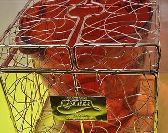 Cubitera Champagne Cattier con un enfriador de vidrio rojo encerrado en una estructura de jaula de alambre metálico dorado.