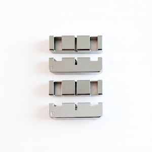 May include: Four silver-colored metal watch link components arranged in two pairs. Each piece features a rectangular shape with two square cutouts and a small letter R engraved on the side. The metallic surface has a smooth, polished finish.