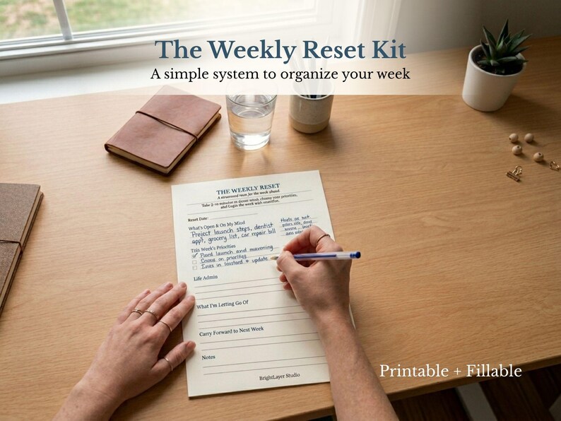 May include: A desk scene featuring a planner titled "The Weekly Reset Kit" with the text "A simple system to organize your week." A person is writing on the planner with a pen. Other items include a leather journal, a glass of water, and a small potted plant.