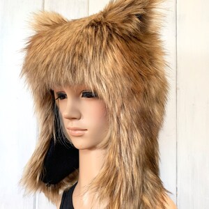 May include: A brown faux fur hat with long, floppy ears. The hat is made of soft, plush fur and has a black lining. The hat is worn by a mannequin with a black tank top.
