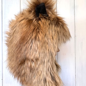 May include: A brown faux fur hat with a black pom-pom on top. The hat has a long, flowing design and is ideal for keeping warm in the winter.