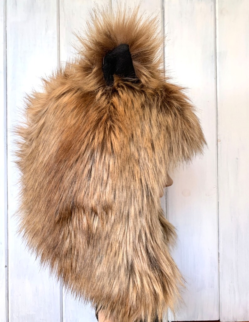 May include: A brown faux fur hat with a black pom-pom on top. The hat has a long, flowing design and is ideal for keeping warm in the winter.