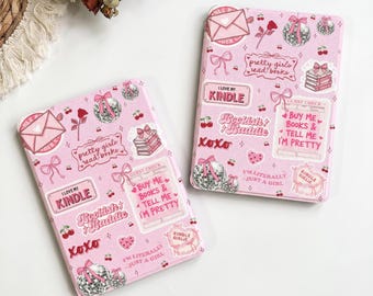 May include: Two light pink e-reader cases featuring a repeating sticker-style pattern of disco balls, bows, cherries, roses, envelopes, and stacks of books. Text includes "I love my Kindle," "Pretty girls read books," and "Buy me books."