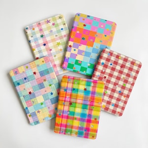 May include: Five rectangular notebooks with rounded corners, each featuring a distinct plaid or checkered pattern in various colors including red, blue, yellow, green, and orange, all overlaid with small, scattered, holographic star-shaped accents.