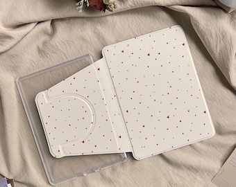 May include: A tablet case featuring a cream-coloured exterior with a pattern of small red hearts. The case includes a clear plastic frame and a folding cover design that allows for multiple viewing angles for the device.