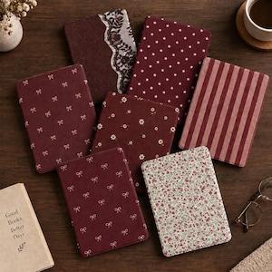 Pode incluir: Uma coleção de sete capas retangulares para leitores digitais em vários tons de bordô e castanho. Os designs incluem estrelas brancas, pequenos padrões florais, riscas finas, laços delicados e uma capa castanha com detalhe de renda.