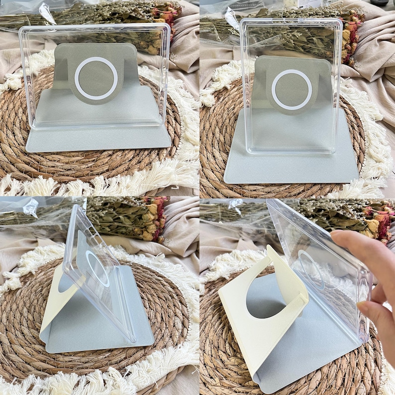 Puede incluir: Un soporte para tel&eacute;fono de acr&iacute;lico transparente con una base de carga magn&eacute;tica gris claro y un dise&ntilde;o de anillo blanco. El soporte cuenta con una base plegable de color gris claro y un marco transparente para dispositivos.