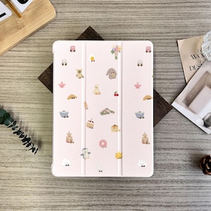 Puede incluir: Una funda para tableta de color rosa claro con un patrón caprichoso de pequeñas ilustraciones coloridas. El diseño incluye imágenes de animales, alimentos y elementos florales. La funda está abierta sobre una superficie de madera.