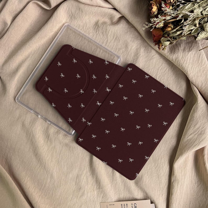 Puede incluir: Una funda para lector electr&oacute;nico o tableta de color granate oscuro con un patr&oacute;n repetitivo de peque&ntilde;os lazos blancos. La funda incluye un marco de pl&aacute;stico transparente y una cubierta granate con una abertura para la c&aacute;mara.