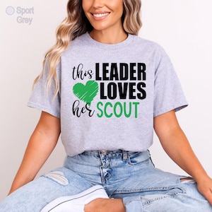 A woman wearing a grey t-shirt with a graphic design that says "this LEADER LOVES her SCOUT" and a green heart symbol.