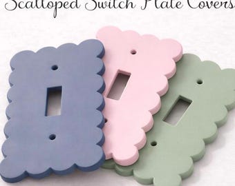 May include: Three rectangular switch plate covers with scalloped edges, featuring a central rectangular cutout and two circular screw holes. The covers are colored in matte blue, light pink, and sage green. The text Scalloped Switch Plate Covers is visible.
