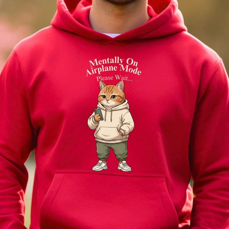 May include: Red hoodie with a front pocket featuring a cartoon cat wearing a hoodie and holding a phone. The cat illustration is paired with the text "Mentally On Airplane Mode Please Wait..."