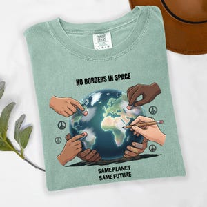 May include: A light green t-shirt with the text "NO BORDERS IN SPACE" above a graphic of the Earth being touched by multiple hands. The text "SAME PLANET SAME FUTURE" is below the graphic. Peace symbols are also visible.