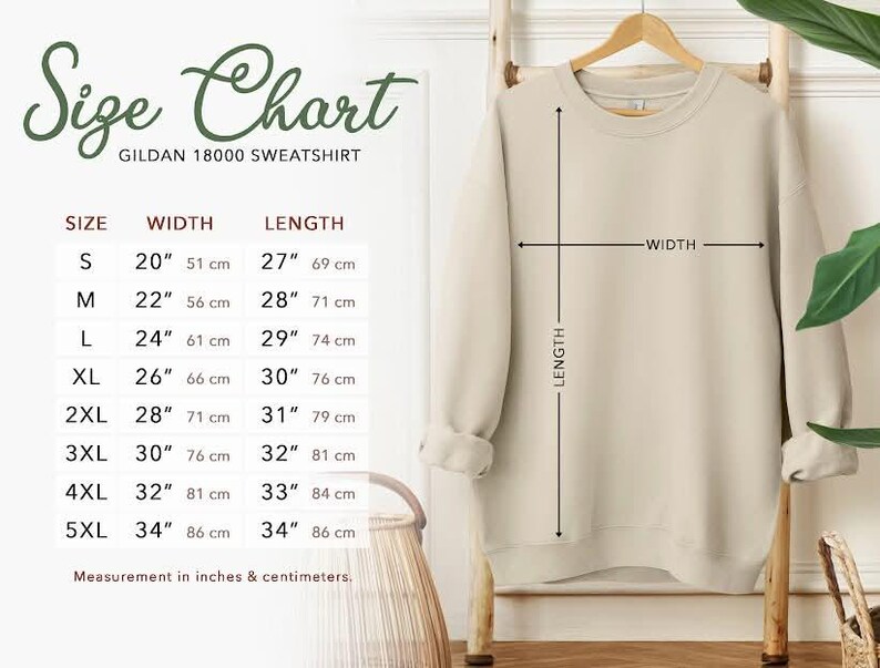 May include: A beige Gildan 18000 sweatshirt hangs on a wooden rack. The image includes a size chart with measurements in inches and centimeters. Sizes range from S (20" width, 27" length) to 5XL (34" width, 34" length).