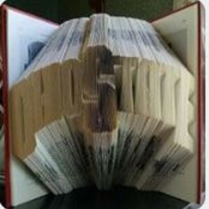 Peut inclure: Une sculpture d'art de livre du mot "PROSPERITY" créée en pliant les pages d'un livre. La sculpture est faite d'un livre brun avec une couverture rouge.