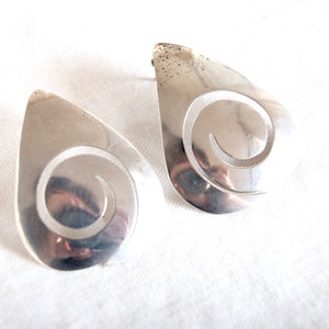 May include: A pair of silver earrings with a teardrop shape and a swirl design.