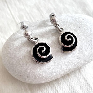 May include: A pair of silver earrings with black enamel swirl designs. The earrings have a post back closure.