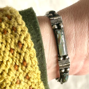 May include: Silver bracelet with a rectangular abalone shell inlay and silver beads. The bracelet is on a person's wrist.