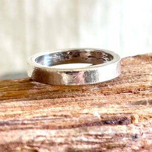May include: A silver ring with a hammered texture, resting on a piece of wood. The ring has a flat band and a slightly irregular surface. The ring is marked with "MEXICO 925".