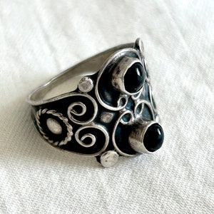 May include: A silver ring with intricate scrollwork and two black gemstones. The ring is designed in a unique, asymmetrical style.