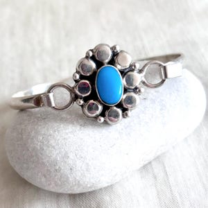 Op de afbeelding: Een zilveren armband met een blauwe turquoise steen gezet in een cirkel van zilveren kralen.