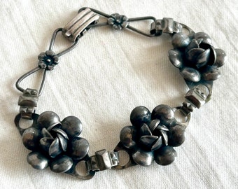 May include: A silver bracelet with three flower-shaped charms. The bracelet has a clasp closure.