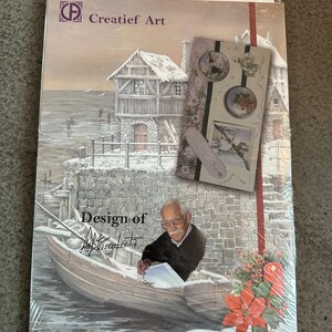 May include: A package of "Creatief Art" art supplies. The cover features a winter scene with a boat, buildings, and an illustration of a man in a boat. The package is wrapped in clear plastic. The design includes the text "Design of" and a signature.