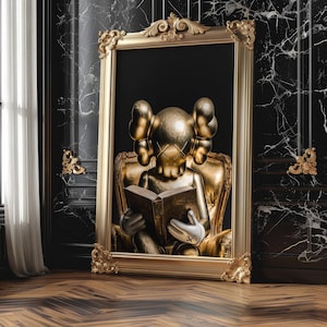Puede incluir: Una obra de arte enmarcada en oro que presenta una figura dorada sentada en una silla dorada, leyendo un libro. La figura tiene orejas grandes y ojos tachados. El fondo es negro.