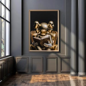 Puede incluir: Una obra de arte enmarcada que presenta una escultura dorada de una figura leyendo un libro mientras est&aacute; sentada en un sill&oacute;n dorado. La obra de arte est&aacute; colocada sobre un fondo negro y enmarcada en un borde dorado. La habitaci&oacute;n tiene paredes grises oscuras y un suelo de madera.